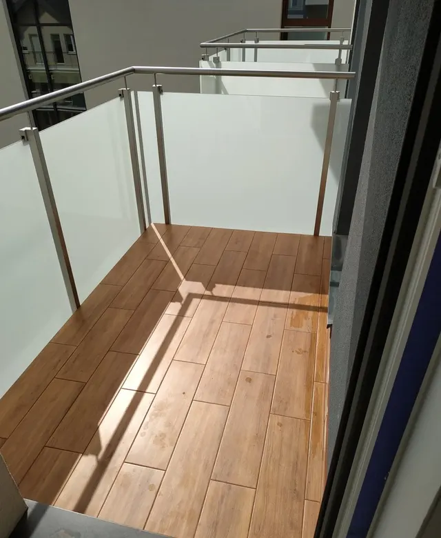 Balkon wykończony płytkami w dekorze drewna ze szklaną balustradą