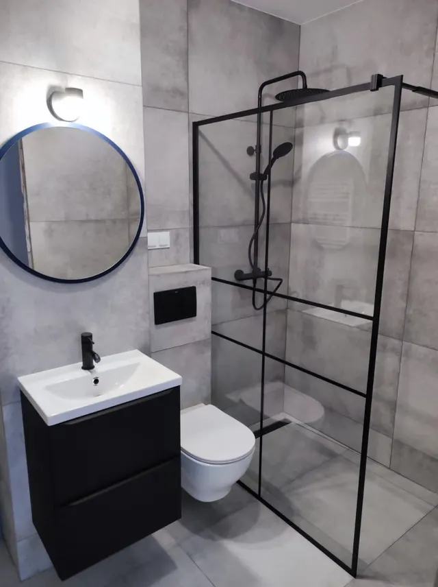 Łazienka w dekorze betonu z czarną kabiną typu walk-in i okrągłym lustrem