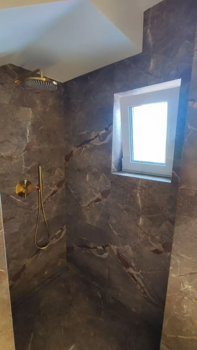 Prysznic w marmurze z oknem i mosiężną baterią podtynkową