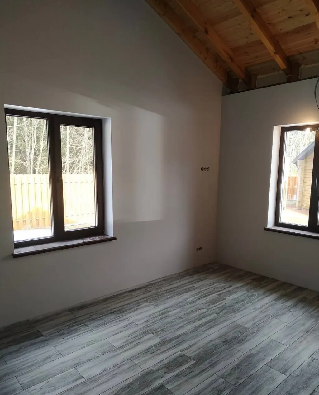 Pokój na poddaszu ze skosem, odsłoniętą konstrukcją drewnianą dachu i podłogą w dekorze szarego drewna