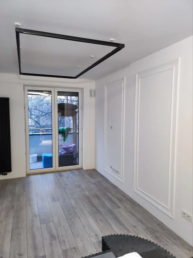Pokój ze sztukaterią na ścianach i czarną ramą na suficie, wyjście na balkon