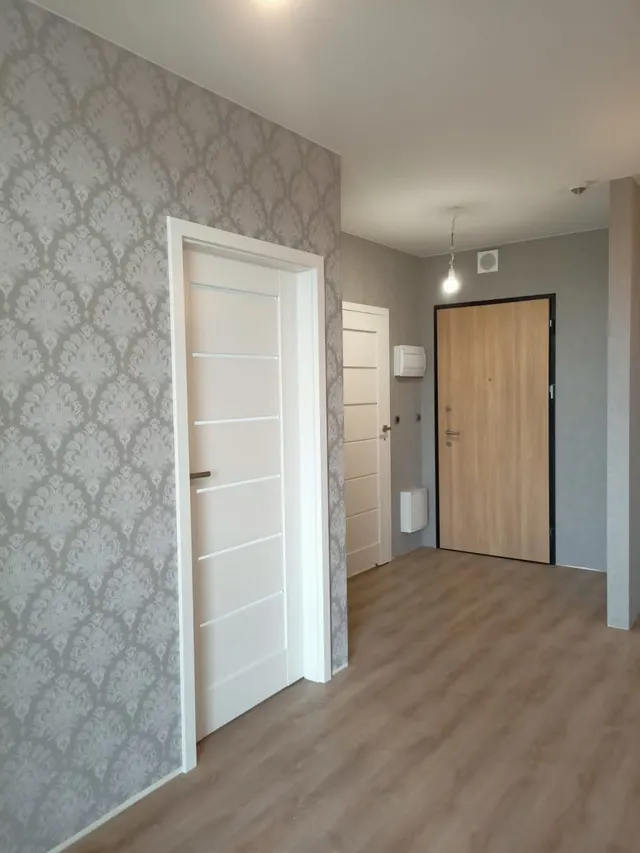 Przedpokój z tapetą w ornamentowy wzór, białymi drzwiami wewnętrznymi i drewnianymi drzwiami wejściowymi