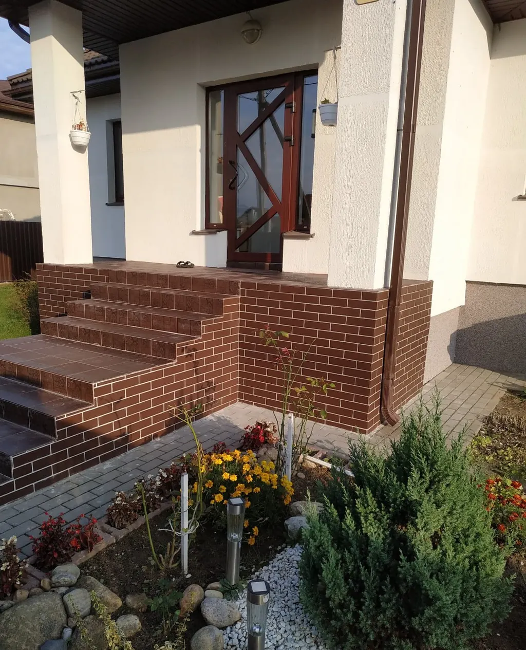 Wejście do domu z klinkierowymi schodami i rabatą z iglakami